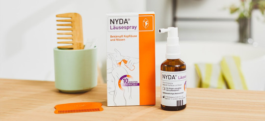 NYDA Läusespray mit Packung, Pumpflasche und orangefarbenem Kamm auf einem hellen Holztisch.