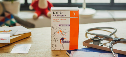 Eine Packung des Nyda-Läusemittels steht auf einem Holztisch. 
