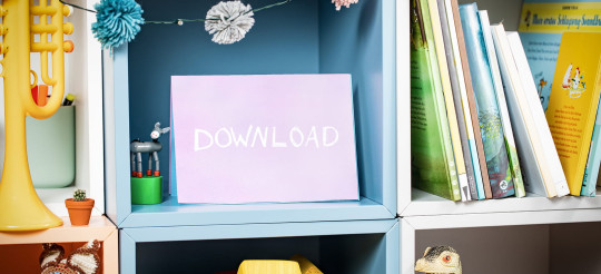 Regal mit Büchern und Schulmaterialien. Auf einem Bildschirm steht das Wort „Download“.