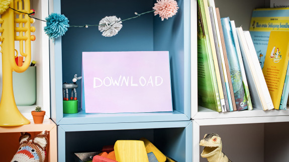 Regal mit Büchern und Schulmaterialien. Auf einem Bildschirm steht das Wort „Download“.