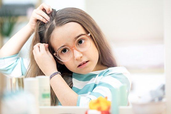 Mädchen mit Brille zieht eine Haarsträhne auseinander und kontrolliert seinen Kopf im Spiegel.