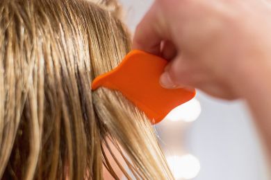 Eine Hand verwendet einen orangen Läusekamm und gleitet durch Haare.