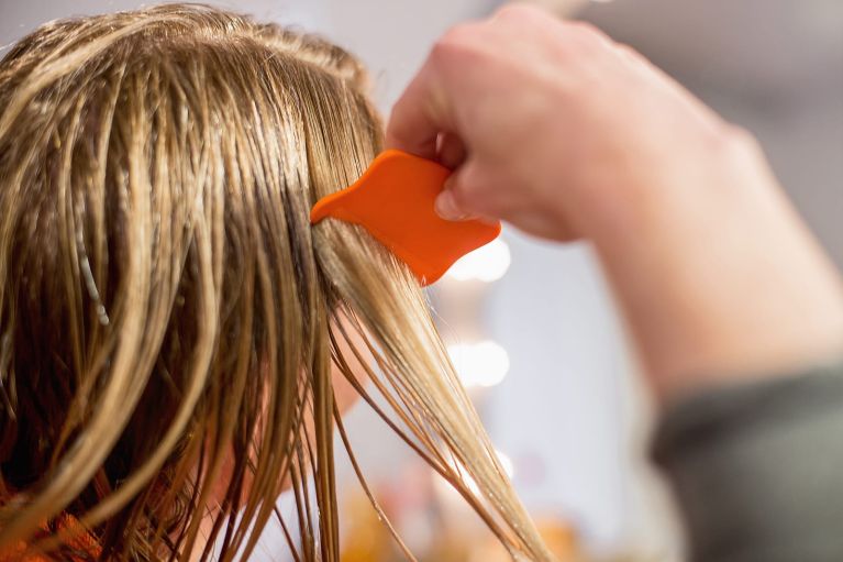 Hand führt einen orangefarbenen Läuse- und Nissenkamm durch eine blonde Haarsträhne.