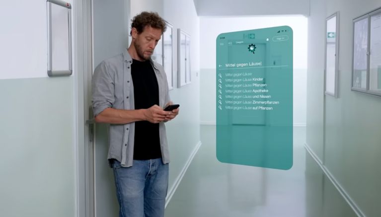 Mann betrachtet sein Smartphone auf in einem hellen Flur.