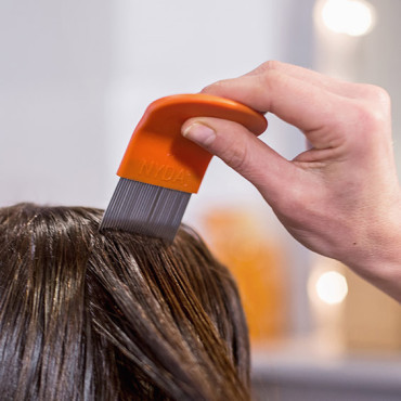 Hand zieht einen orangefarbenen Läuse- und Nissenkamm durch eine nasse dunkle Haarsträhne.