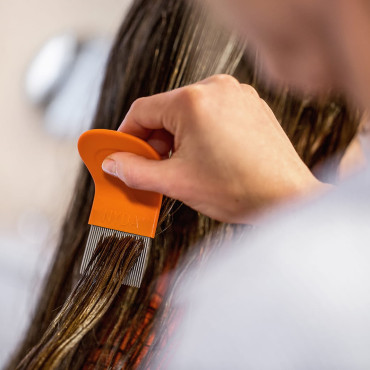 Hand führt einen orangefarbenen Läuse- und Nissenkamm nah an der Kopfhaut durch langes Haar.
