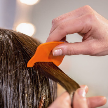 Hand zieht einen orangefarbenen Läuse- und Nissenkamm durch eine nasse dunkle Haarsträhne.