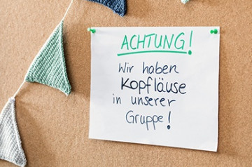 Notizzettel „Achtung! Wir haben Kopfläuse in unserer Gruppe!“ hängt mit Nadeln an einer Pinnwand.