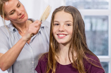 Frau kämmt mit einer Haarbürste das lange Haar eines lächelnden Mädchens.