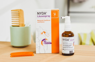 NYDA Läusespray mit Packung, Pumpflasche und orangefarbenem Kamm auf einem hellen Holztisch.