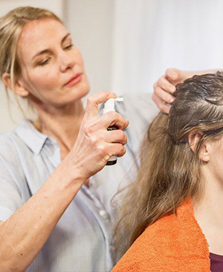 Eine Frau sprüht einem Mädchen NYDA® Läusespray auf den Haaransatz.
